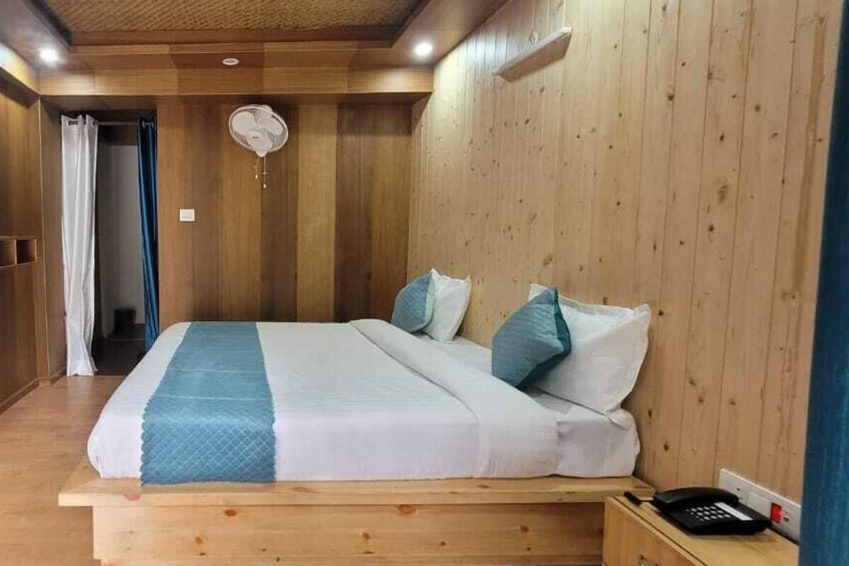A bedroom with a wooden bed, a bedside table, a fan, and a view of a balcony.