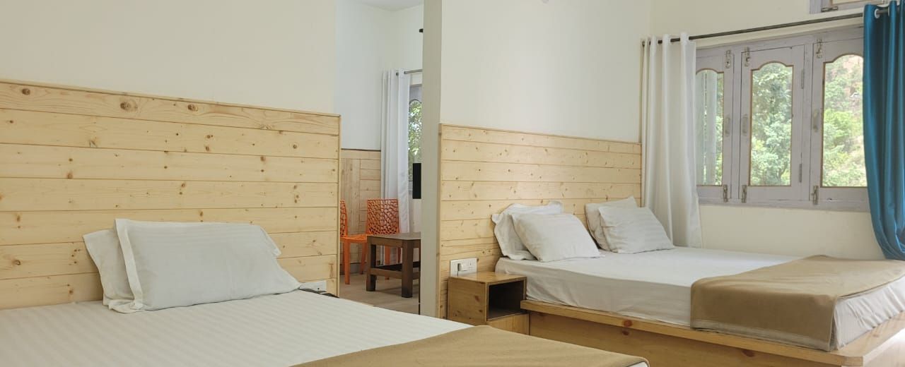 A room with two beds, wooden headboards, a small table, and a window with curtains.