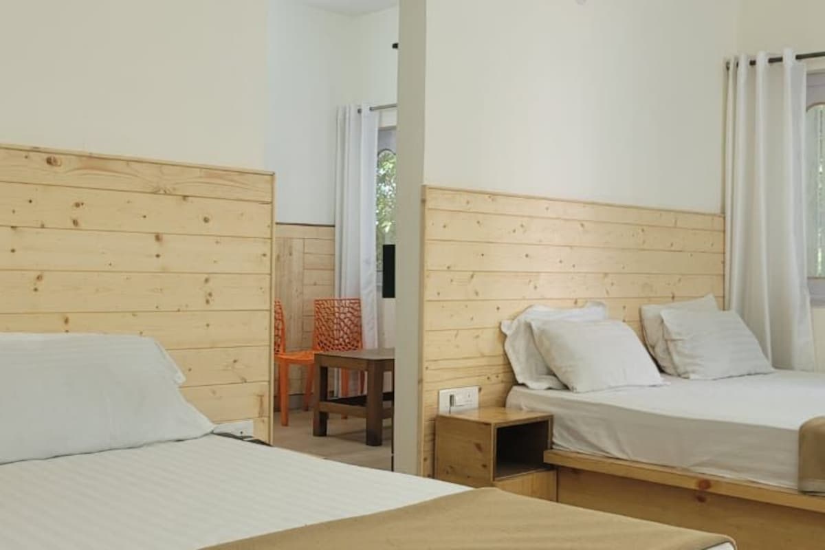 Ein Zimmer mit zwei Betten, Holz-Kopfteilen, einem kleinen Tisch und einem Fenster mit Vorhängen.