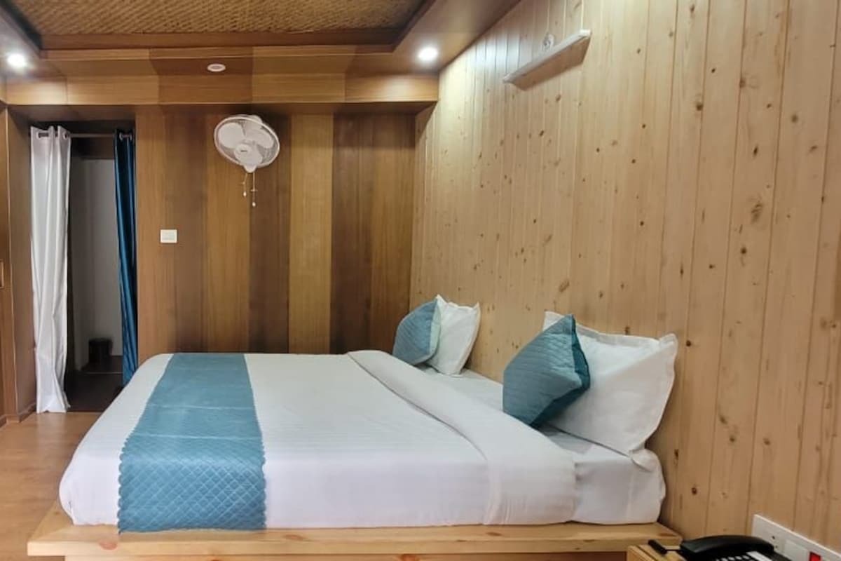 Ein Schlafzimmer mit einem hölzernen Bett, einem Nachttisch, einem Ventilator und Blick auf einen Balkon.
