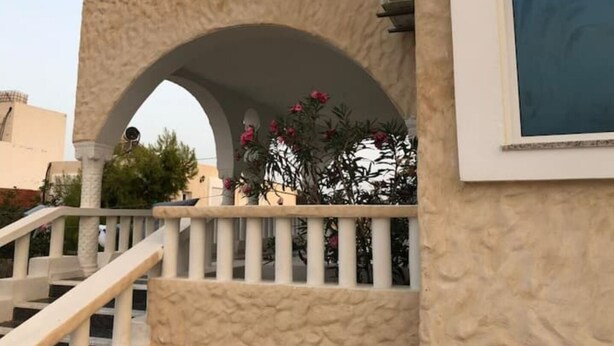 Un immeuble doté d’une façade beige à texture marquée, d’une balustrade de balcon blanche et d’un escalier menant à un étage supérieur.