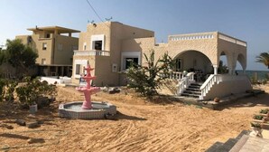 Un bâtiment moderne doté d’un toit plat, d’une fontaine rose et d’un escalier menant à une zone abritée.