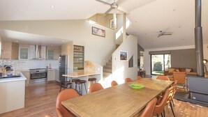 Et rummeligt køkken med moderne hårde hvidevarer, et spiseområde med et træbord og orange stole, samt en stor pejs.