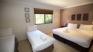 A hotel room with two single beds, a large bed, a window with blinds, and three framed pictures on the wall.