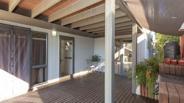 A covered outdoor area with a wooden deck, a barbecue grill, and a table with chairs.