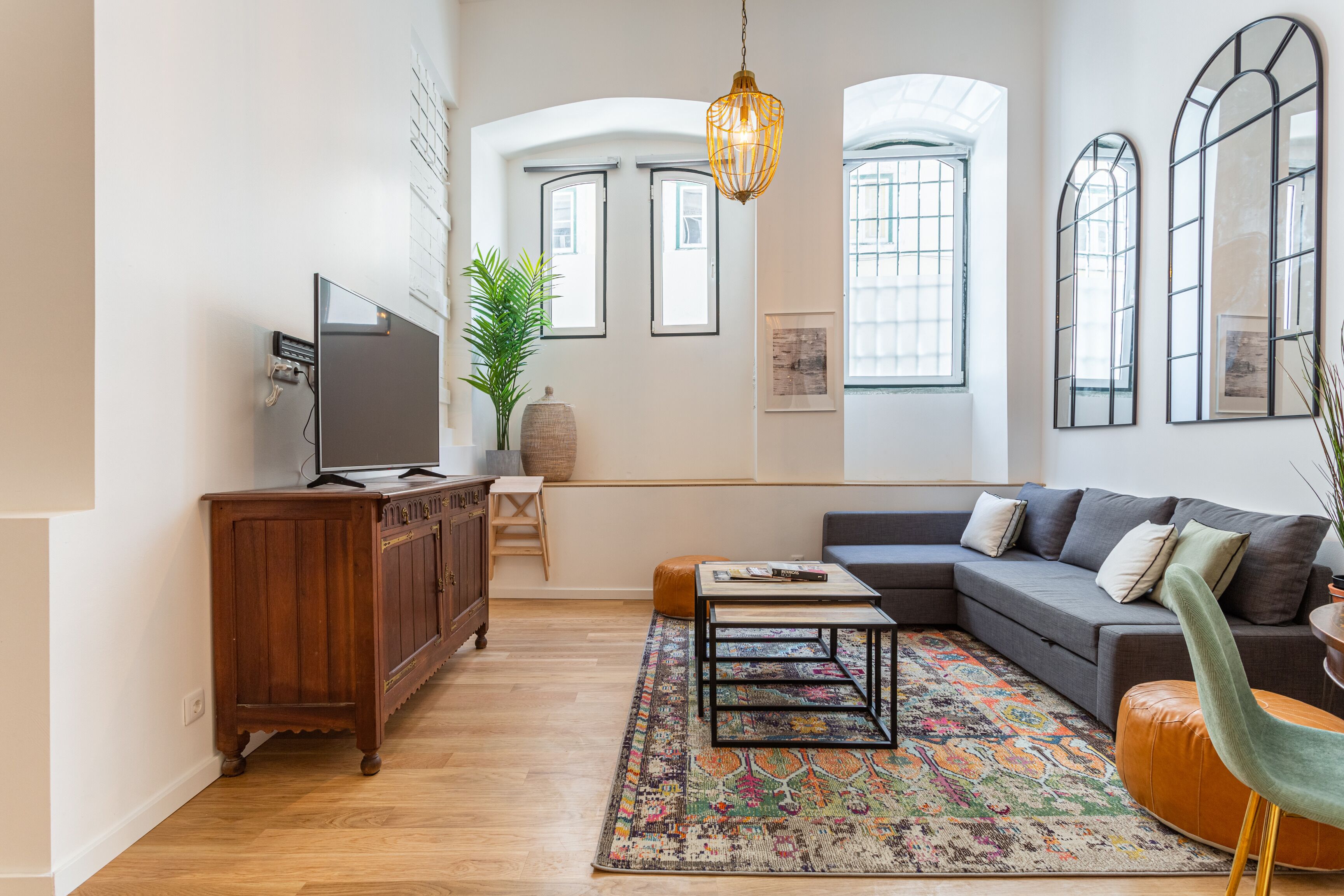 A modern living room with a sectional sofa, a coffee table, a television on a wooden cabinet, and a patterned rug.