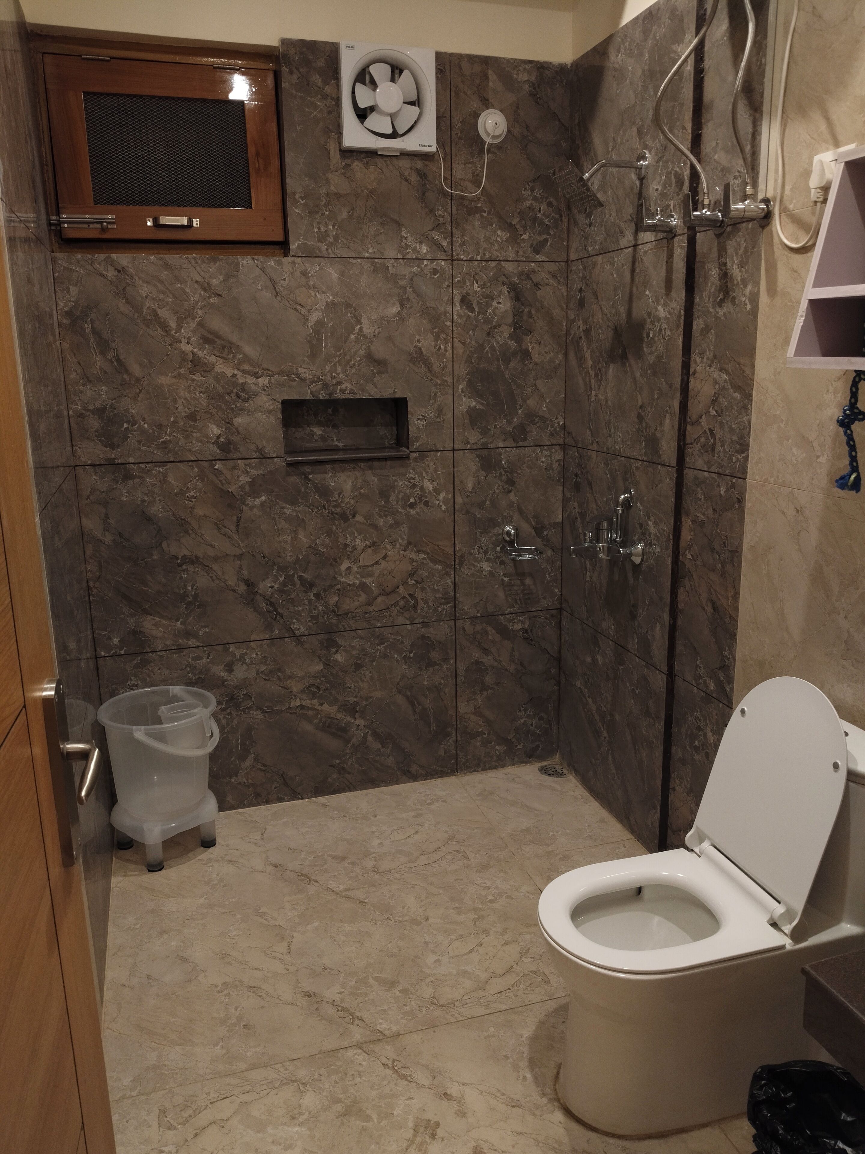 A bathroom with a toilet, a shower, and a built-in fan.