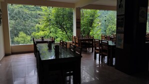 A dining area with tables and chairs, large windows with a view of greenery, and motivational posters on the walls. - Harela Inn – A Boutique Himalayan Wedding Retreat (Chamoli)