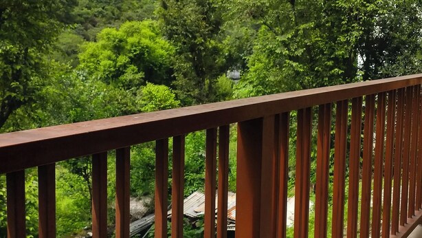 A balcony with a metal railing overlooking a lush green landscape and mountains in the distance. - Harela Inn – A Boutique Himalayan Wedding Retreat (Chamoli)