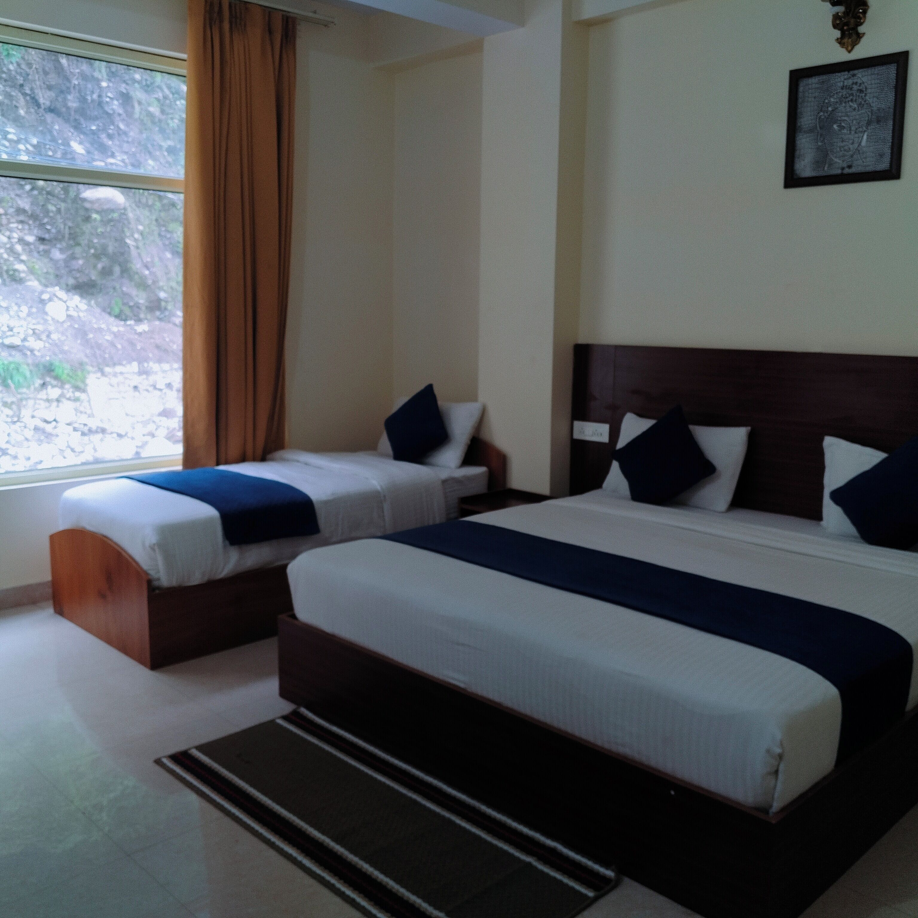 A hotel room with two beds, a window with curtains, a framed picture on the wall, and a wooden headboard.