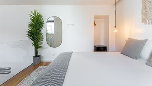 Ein modernes Schlafzimmer mit einem großen Bett, einem Blumentopf, einem Spiegel und einem Nachttisch mit Lampe.