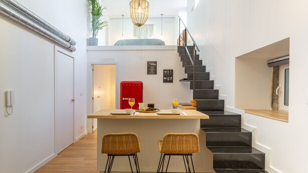 Eine moderne Küche mit einer zentralen Kochinsel, zwei Barhocker, einem roten Kühlschrank und einer Treppe zu einer oberen Ebene.