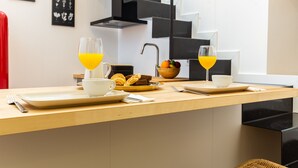 Ein Frühstücksarrangement mit zwei Orangensäften, einer Obstschale und Croissants auf einem Holztisch in einer modernen Küche mit einer Treppe im Hintergrund.