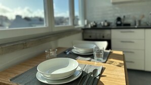 A dining table with plates, cutlery, and glasses, set in a modern kitchen with white cabinets and a view of mountains through a large window. - Studio 59 Lisboa (Lisbon)