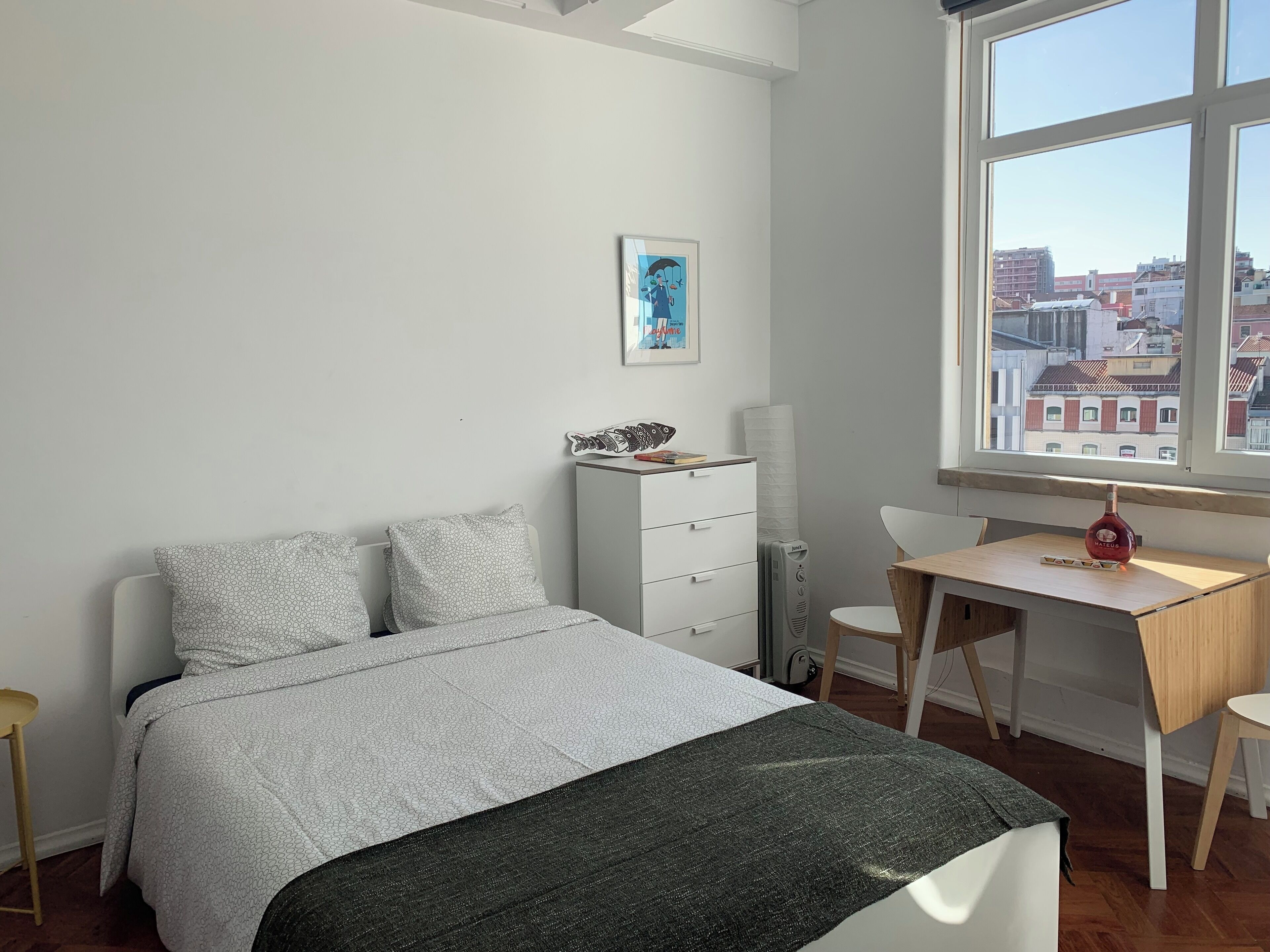 A bedroom with a bed, a desk, and a window with a city view.