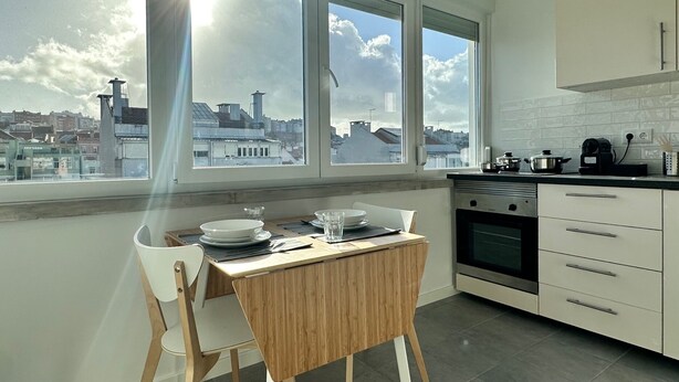 A modern kitchen with a dining table and chairs, large windows with a city view, and a built-in oven. - Studio 59 Lisboa (Lisbon)
