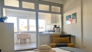 A modern hotel room with a bed, a small table with chairs, a kitchen area visible through a glass door, and a painting on the wall. - Studio 59 Lisboa (Lisbon)