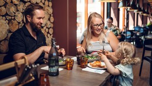 A family dining at a restaurant with a wooden log wall and modern pendant lighting.