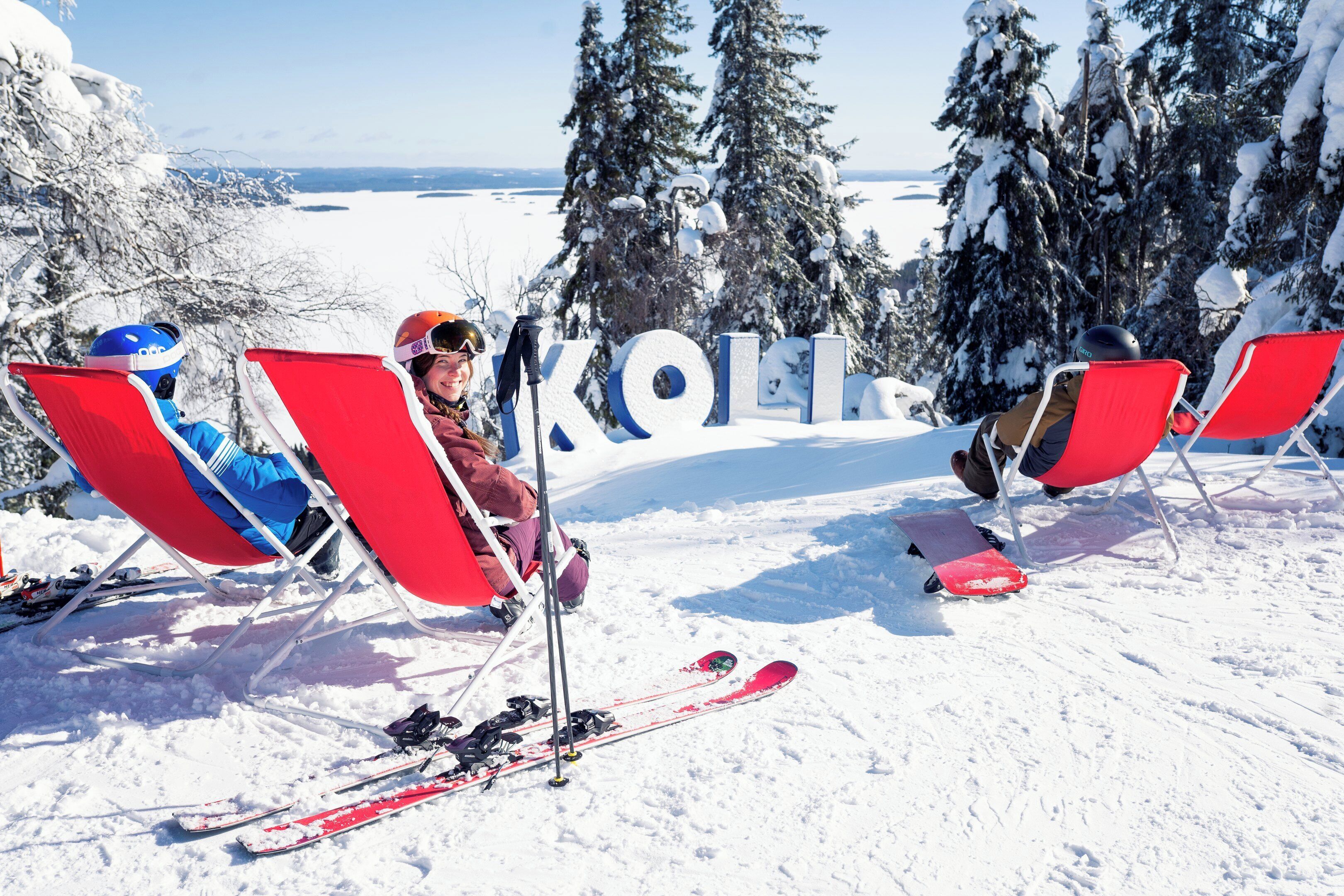 Two red chairs with skis and poles, a snow-covered landscape, and the word "KOLL" in the background.