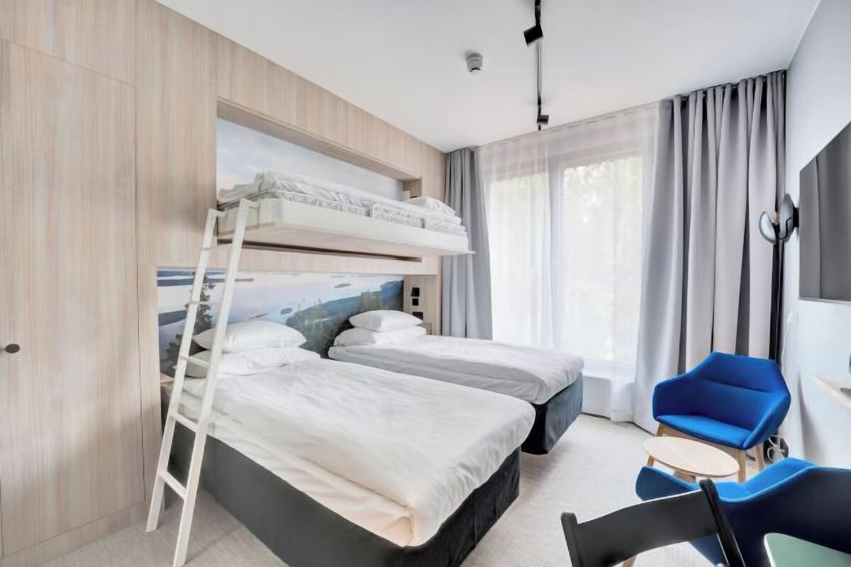Habitación de hotel con literas, un escritorio, una silla y un ventanal grande con cortinas.