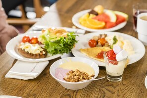 A wooden table with various breakfast dishes including a salad, omelette, and a dessert with strawberries and yogurt. - Break Sokos Hotel Koli Kylä (Lieksa)