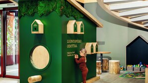 A child interacting with a green playhouse with wooden birdhouses and a circular mirror.