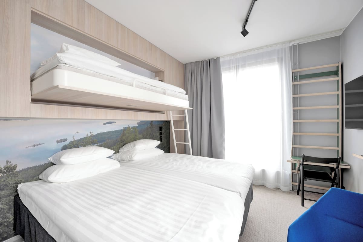 Ein Hotelzimmer mit einem Etagenbett, einem Schreibtisch, einem Stuhl und einem großen Fenster mit Vorhängen.
