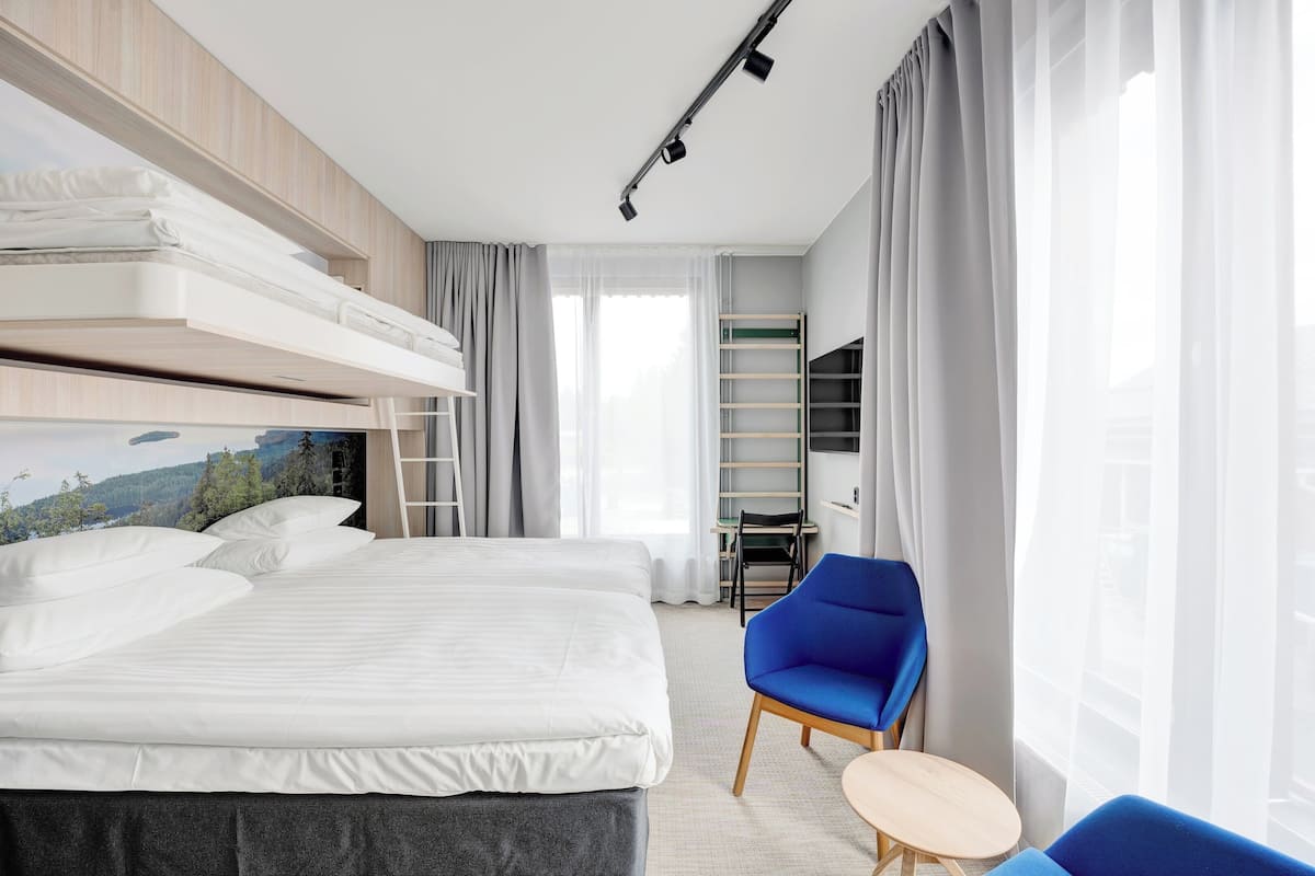 Ein modernes Hotelzimmer mit einem großen Bett, einem Schreibtisch, einem Sessel und einem Fernseher.
