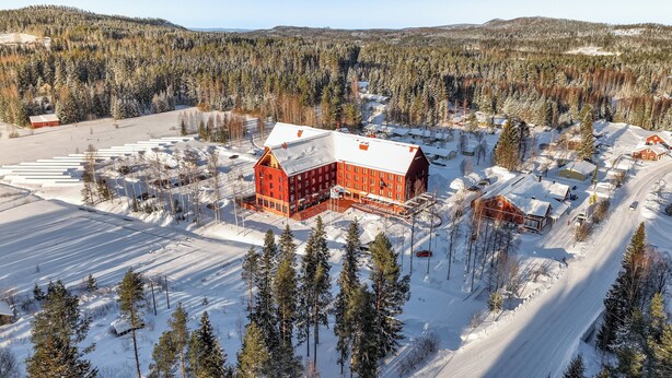 A large red barn with a snow-covered roof, surrounded by a parking lot and a forested area.
