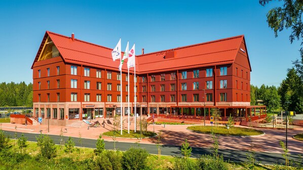 A large red building with multiple floors, a covered entrance area, and several flags. - Break Sokos Hotel Koli Kylä (Lieksa)