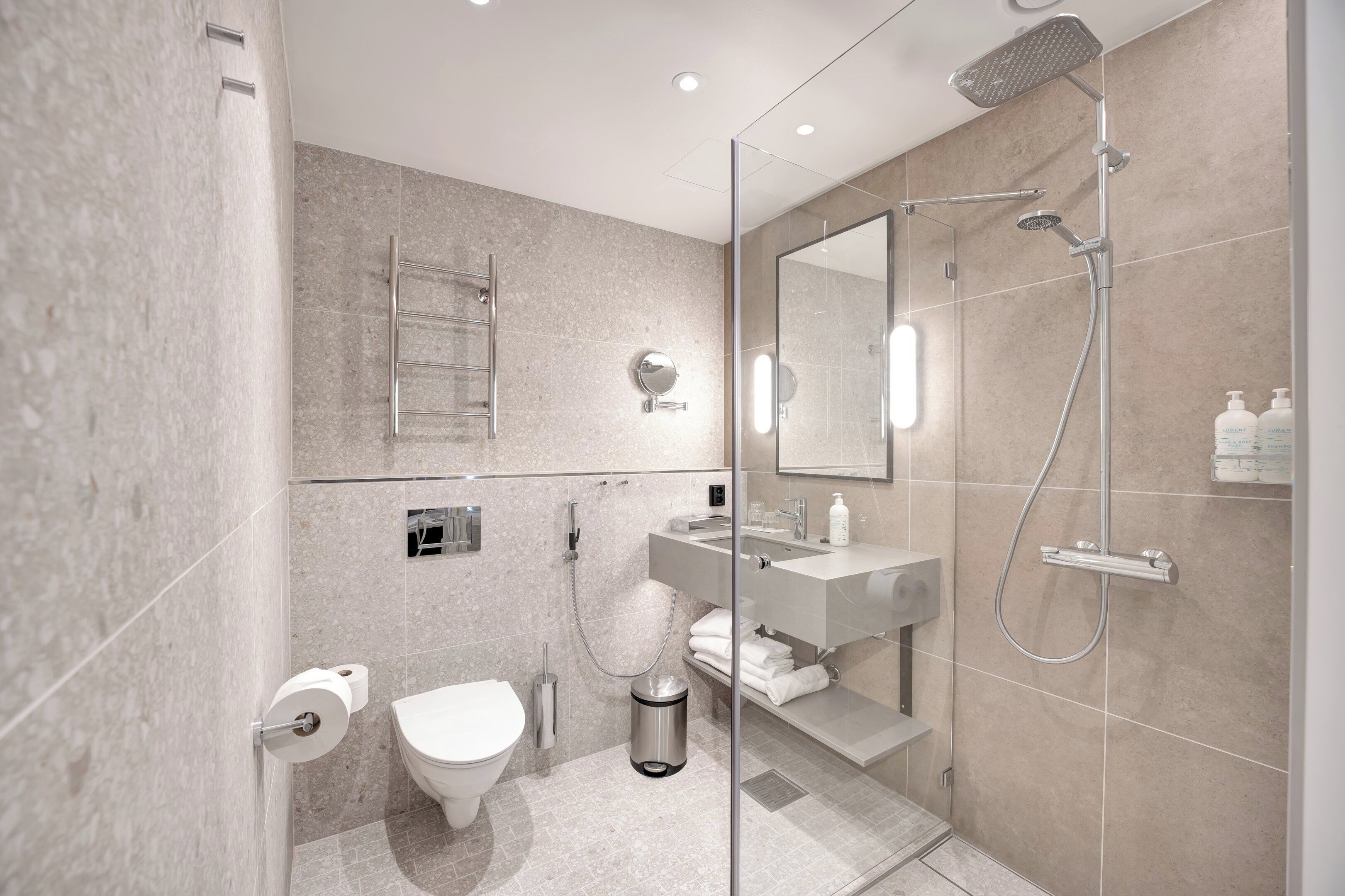 Ein modernes Badezimmer mit Duschkabine aus Glas, Toilette, Waschbecken und Spiegel.