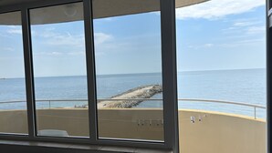 A room with large windows overlooking a coastal area with a rocky shoreline and calm sea. - Panorama-apartmentsChantall (Ravda)