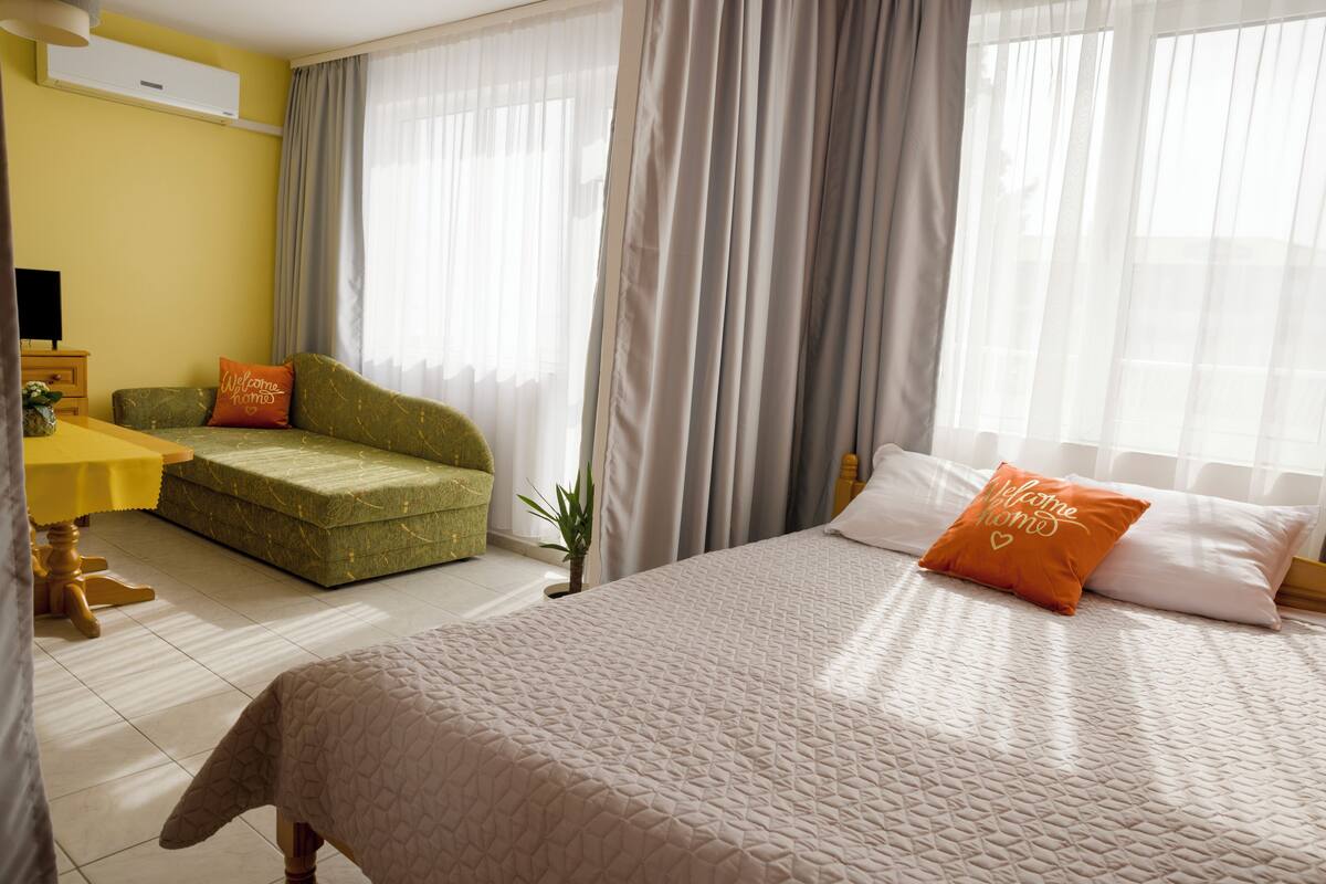 A hotel room with a bed, a sofa, a small table, and curtains.