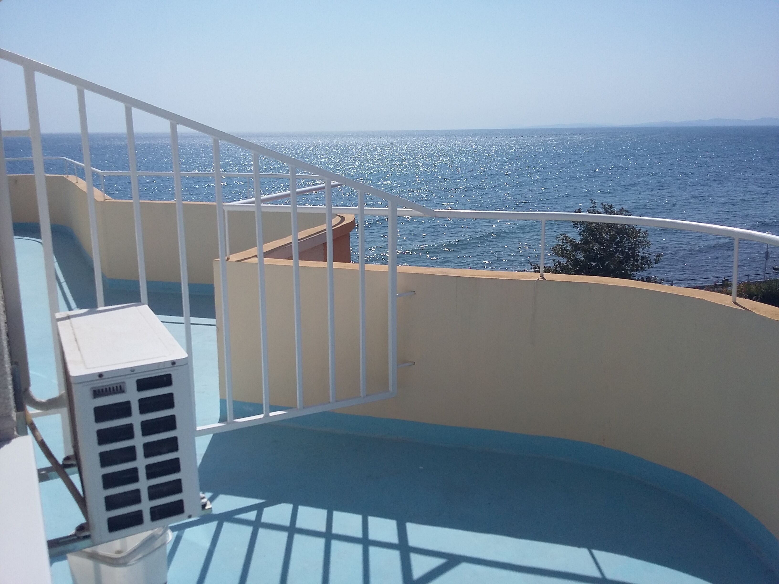 A balcony with a view of the sea, a white railing, and a beige wall.