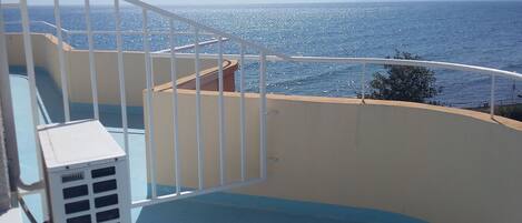 A balcony with a view of the sea, a white railing, and a beige wall.