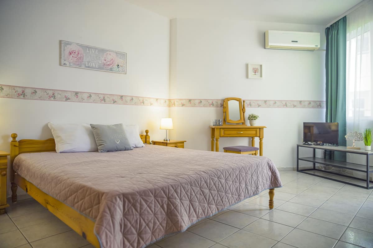 A bedroom with a bed, bedside tables, a mirror, a TV stand, and an air conditioning unit.