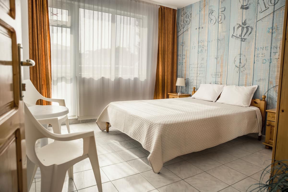 A hotel room with a bed, a chair, a small table, and a window with curtains.
