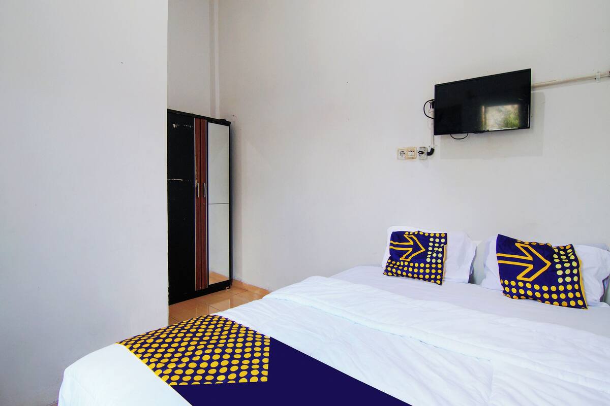Ein Hotelzimmer mit einem Bett, zwei Kissen mit Pfeilmuster, einem an der Wand befestigten Fernseher und einem Kleiderschrank.