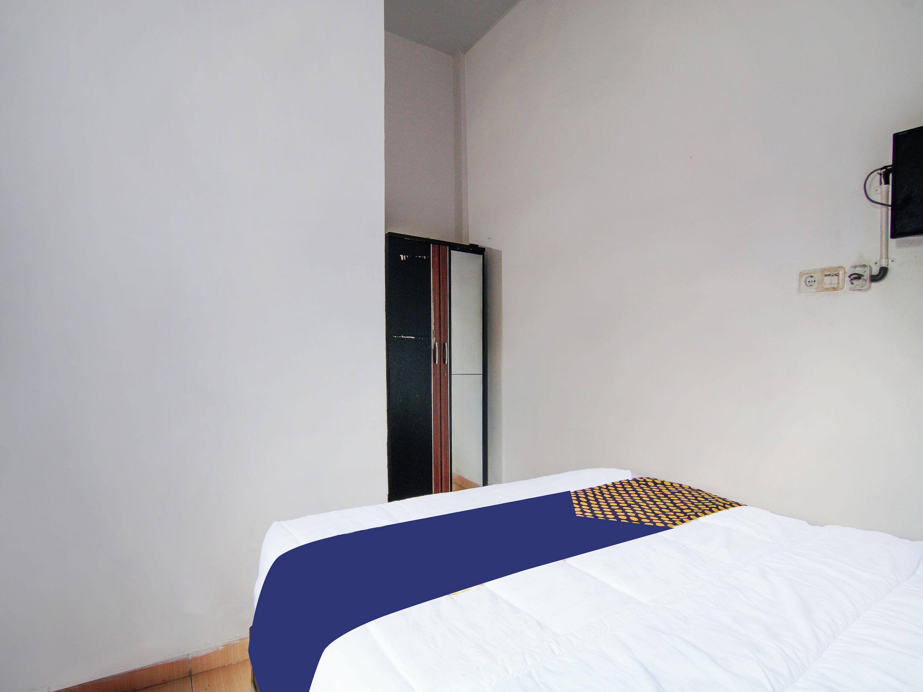 A hotel room with a bed, a wardrobe, and a television mounted on the wall.