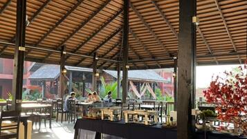 An outdoor dining area with tables and chairs, a covered roof, and a view of buildings in the background.
