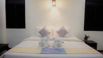 Una cama bien tendida con ropa de cama blanca, dos almohadas con diseño de cielo, una mesita de noche con una planta y una lámpara de pared.
