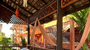 A traditional wooden structure with a thatched roof, a staircase, and a bed with a red and white bedspread. - Rainforest Huahin Village Hotel (Hua Hin)