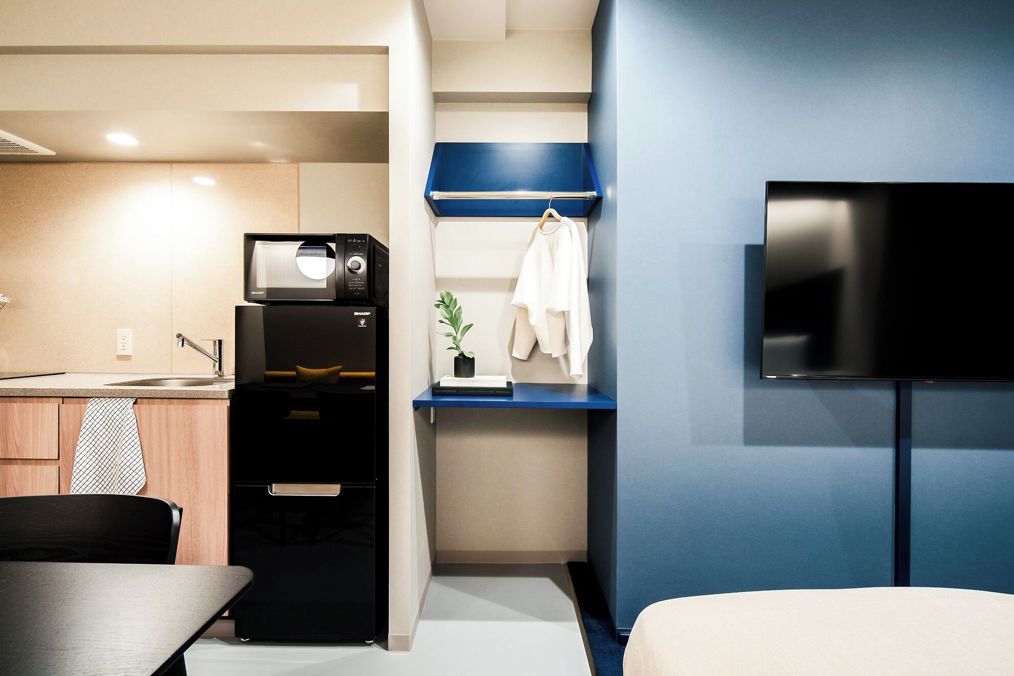 A compact living space with a kitchenette, a flat-screen TV mounted on the wall, and a small seating area.