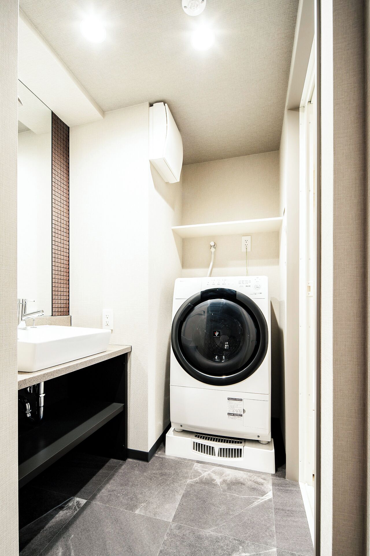 A compact hotel bathroom with a sink, mirror, and a front-loading washing machine.