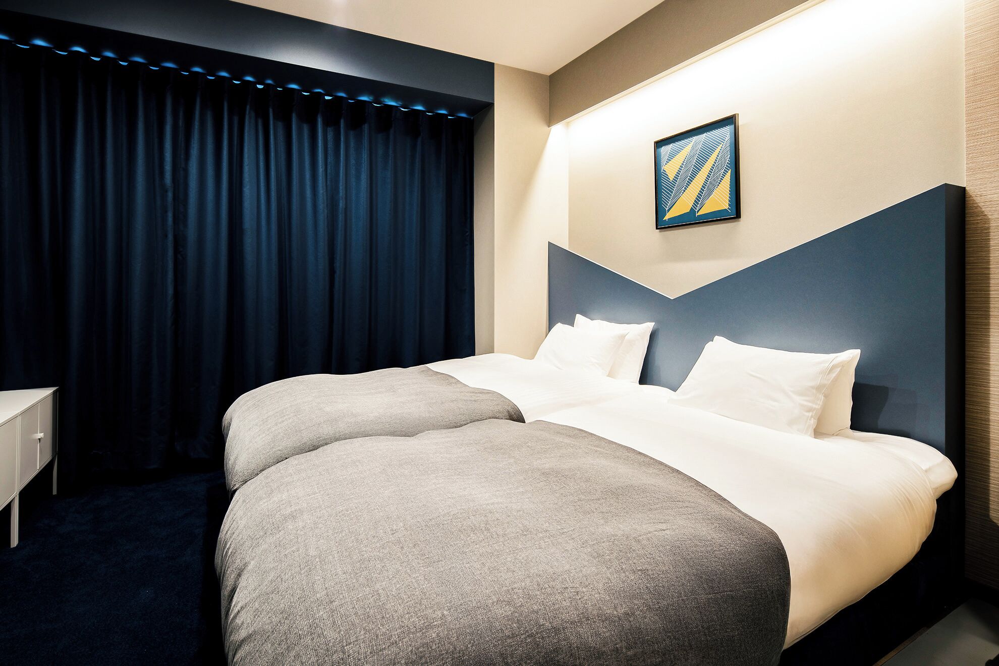 A hotel room with a large bed, a headboard, a nightstand, and a window with curtains.