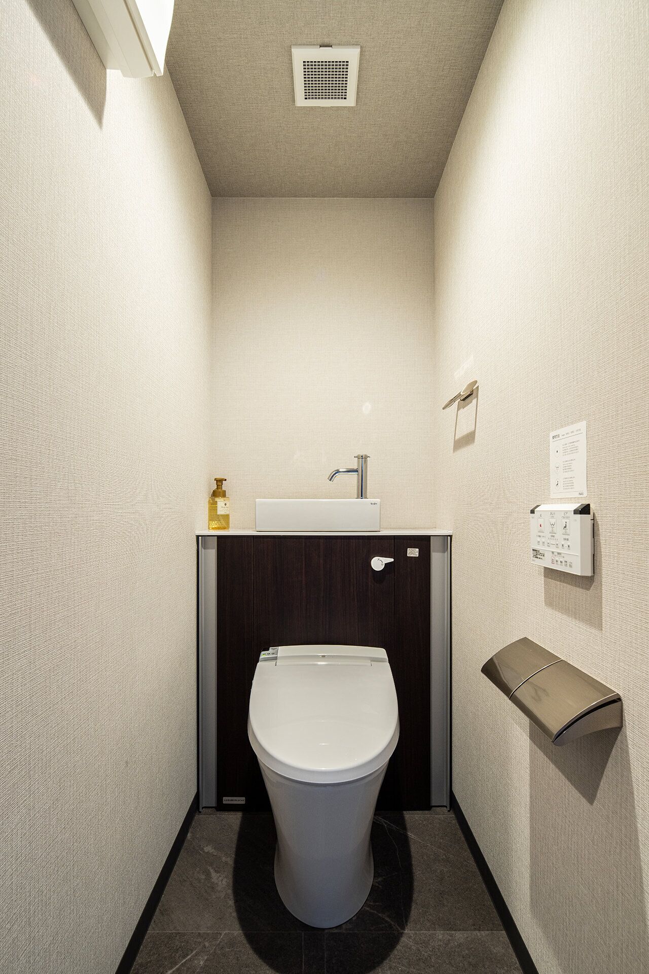 A small, modern bathroom with a toilet, sink, and a towel dispenser.