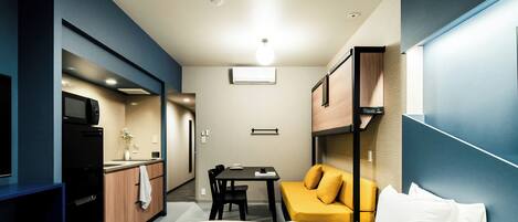 A compact hotel room with a bed, a small table, a sofa, a microwave, and a sink.