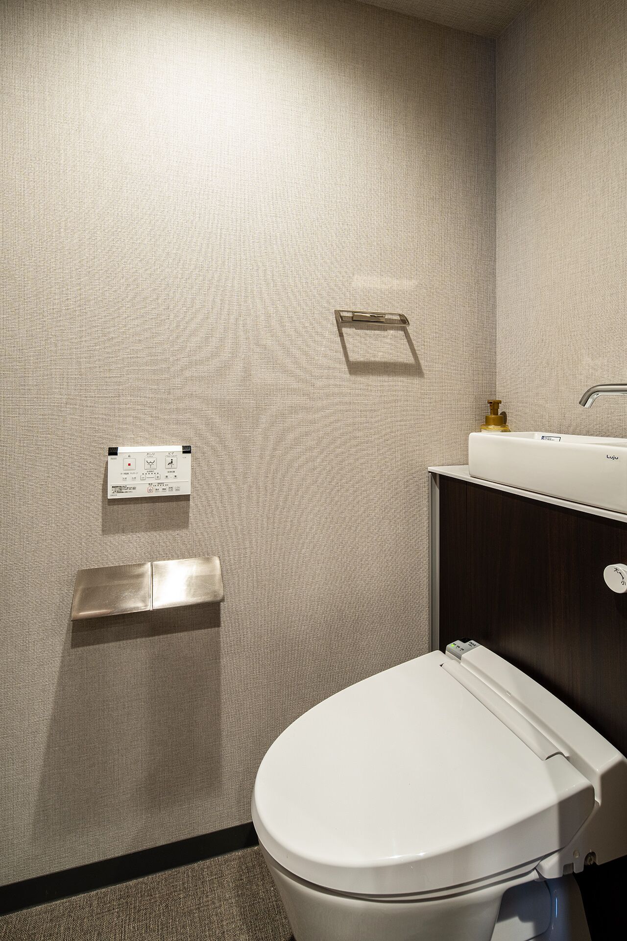 A modern bathroom with a white toilet, a wall-mounted sink, and a control panel.