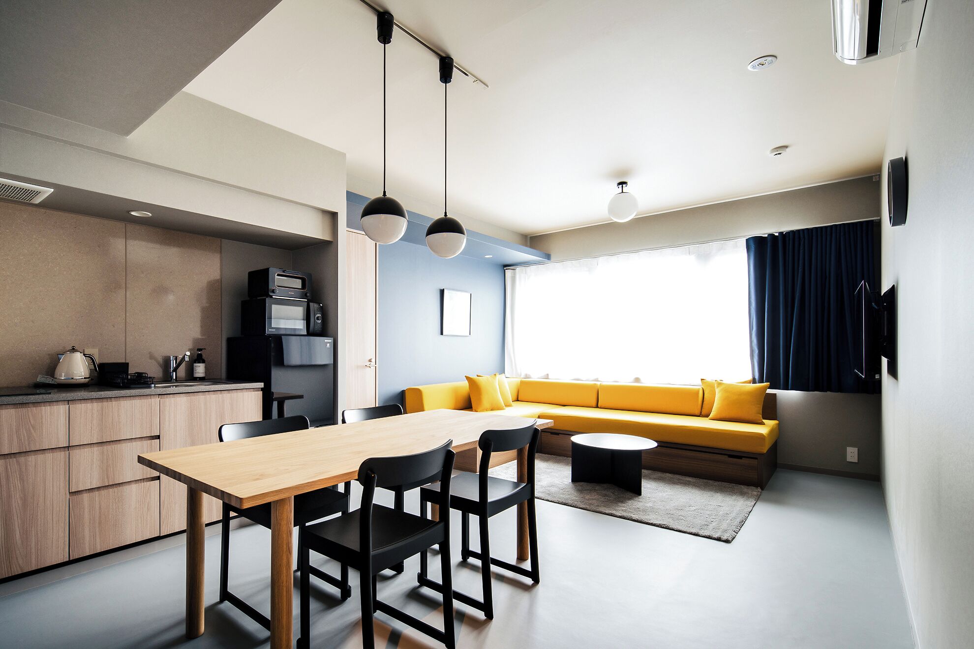 Una cocina moderna con comedor, un sofá amarillo y un ventanal grande.