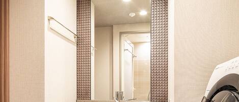 Un baño de hotel con un espejo grande, un lavamanos, una lavadora y un perchero para toallas.